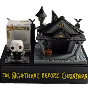 May include: A black display featuring a Jack Skellington Funko Pop figure and a miniature haunted house. The display includes the text "THE NIGHTMARE BEFORE CHRISTMAS" in yellow lettering. A pumpkin is on the porch of the house.