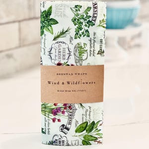 May include: Beeswax bread wrap with a botanical design featuring herbs and the text "Wind & Wildflowers." The wrap is 17x21 inches and has a brown paper band.