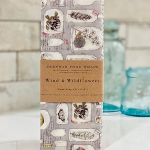 May include: Beeswax food wrap in a gray and white pattern with a floral and feather design. The wrap is labeled "Wind & Wildflowers" and "Bread Wrap XXL (17x21)".