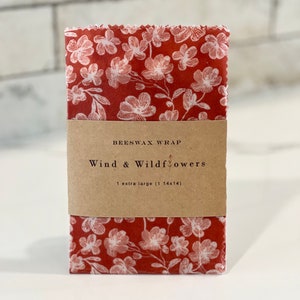 May include: A red beeswax food wrap with a white floral pattern. The wrap is labeled "Beeswax Wrap Wind & Wildflowers 1 extra large (14x14)"