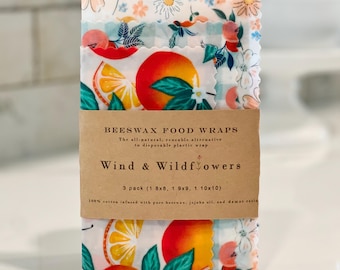 May include: Three reusable beeswax food wraps with floral and fruit designs. The wraps are secured with a brown paper band that reads "Wind & Wildflowers." The wraps measure 20x20, 23x23, and 25x25 cm.
