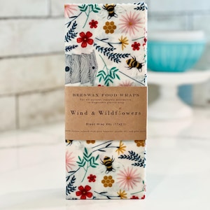 May include: A set of three beeswax food wraps with a floral and bee design. The wraps are labeled "Wind & Wildflowers" and "Bread Wrap XXL (17x21)".