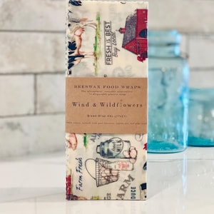 May include: Beeswax food wraps in a bread wrap size, featuring a farm-themed design with a red barn, cows, and a milk jug. The label reads "Beeswax Food Wraps", "Wind & Wildflowers", and "Bread Wrap XXL (17x21)".