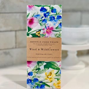 May include: Beeswax food wraps with a floral design. The wraps feature a white background with pink, blue, and yellow flowers. The packaging reads "Wind & Wildflowers" and "Bread Wrap XXL (17x21)".