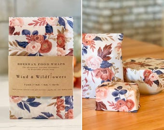 May include: Reusable beeswax food wraps with a floral pattern in pink, red, and blue. The wraps are labelled "Wind & Wildflowers" and come in a 3-pack with sizes 20x20, 23x23, and 25x25 cm. An all-natural, reusable alternative to plastic wrap.