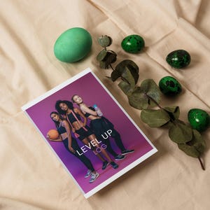Puede incluir: Un folleto morado con el texto "LEVEL UP LOG" en la portada. Cuatro mujeres aparecen en la portada, vestidas con ropa de entrenamiento y sosteniendo equipo de ejercicio. El folleto está rodeado de huevos de Pascua moteados de verde y una rama de eucalipto.