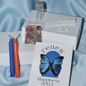 May include: A collection of spiritual items, including two candles, a small glass bottle, a packet of dried herbs, a selenite wand, a crystal, and a card with a blue butterfly and the word "renew". The candles are blue and orange.