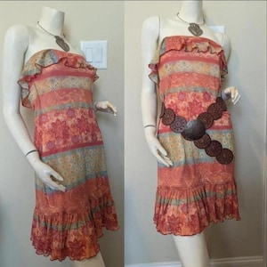 May include: A strapless, knee-length dress with a floral and geometric pattern in shades of orange, red, and blue. The dress features a ruffled neckline and hem. A brown belt with circular accents is worn around the waist.