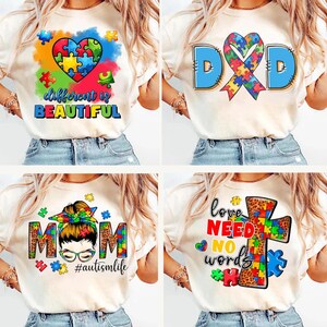 K&ouml;nnte beinhalten: Vier wei&szlig;e T-Shirts mit verschiedenen Designs, die ein Puzzle-Herz, ein blaues Band mit Puzzleteilen, eine Frau mit Dutt und Brille sowie ein Kreuz mit Puzzleteilen zeigen. Der Text auf den Shirts lautet "different is beautiful", "DAD", "MOM #autismlife" und "love need no words".
