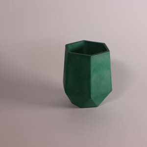 May include: A green geometric planter made of concrete. The planter has a hexagonal shape and a smooth, matte finish.