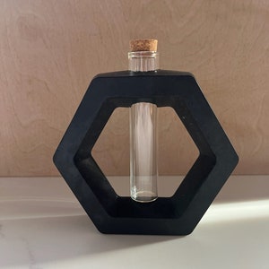 May include: A black hexagonal vase with a glass test tube inside. The test tube has a cork stopper.