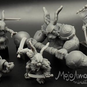 May include: A set of grey painted miniature figurines of rabbit-like creatures, some with swords and shields, others with a staff and a ball. The miniatures are part of a tabletop game called "Dice Heroes".