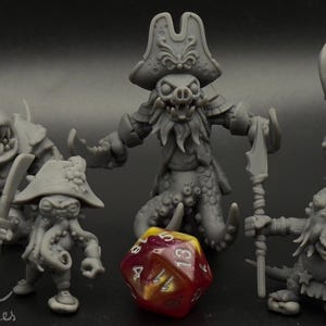 May include: Five grey painted miniature figurines of fantasy creatures, including a pirate with a tentacle beard, a crab-like creature, and a creature with a spiked head. A red and yellow dice is in the center of the image. The text "Dice Heads" is in the top left corner of the image.