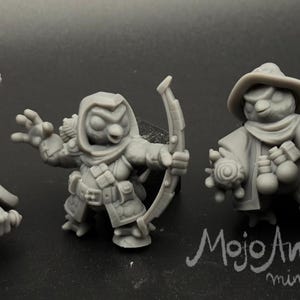 May include: Four gray miniature figurines of fantasy characters. One figure wields a sword and hammer, another a bow and arrow, a third a staff, and the last a trident and shield. The Dice Heads logo is in the upper left corner.