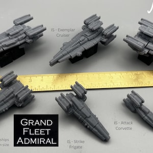 May include: A collection of gray miniature spaceship models, including a System Guardian, Exemplar Cruiser, and Galactic Explorer. A ruler and a twenty-sided die are also present. The text "Grand Fleet Admiral" is displayed.