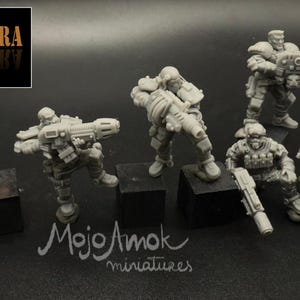 May include: Six gray miniature figures in various action poses, each holding a weapon. The figures are on small black platforms. The image includes the text "EN COBERTURA" and "Single-piece figures in 6 poses."
