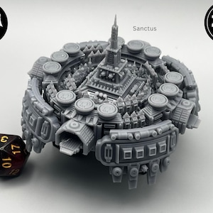 May include: A detailed gray miniature model of a fortress, labeled "Sanctus", with a central tower and surrounding structures. A multi-sided die rests beside the model. The image includes "Flea Market" and "ZBS miniatures" logos.