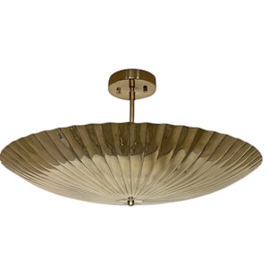 May include: A brass-colored ceiling light fixture with a large, scalloped shade. The shade has a ribbed design, and the fixture is mounted on a short stem with a circular base. The light is a decorative element for home decor.