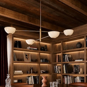 May include: A modern chandelier featuring a central brass rod with four extending arms, each holding a white, bowl-shaped glass shade. The fixture is suspended from the ceiling, providing downward illumination with its sleek, metallic finish.