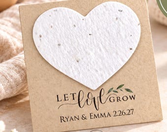 May include: A square kraft paper card featuring a white heart-shaped plantable seed paper. The card displays the text "LET LOVE GROW" above "RYAN & EMMA 2.26.27" and includes a circular graphic stating "INCLUDES 2" PLANTABLE SEED HEART".