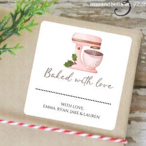 May include: A gift tag with a pink stand mixer illustration and the text "Baked with love." The tag is on a wrapped package with a sprig of greenery and red berries. The text "Holiday Mixer Style #1" is also visible.