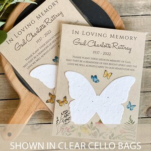 Peut inclure: Deux cartes en papier de graines en forme de papillon blanc avec une bordure florale et un message qui dit "En souvenir affectueux Gail Charlotte Rattray 1937-2022 Veuillez planter ces graines en m&eacute;moire de Gail, qu'elles soient un rappel de son esprit lumineux et de l'amour que nous porterons toujours dans nos c&oelig;urs pour elle."