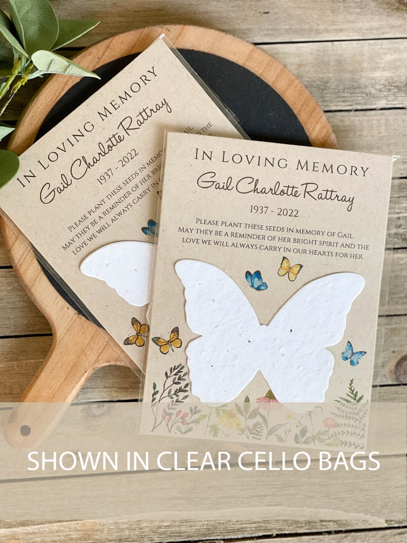 Peut inclure: Deux cartes en papier de graines en forme de papillon blanc avec une bordure florale et un message qui dit "En souvenir affectueux Gail Charlotte Rattray 1937-2022 Veuillez planter ces graines en m&eacute;moire de Gail, qu'elles soient un rappel de son esprit lumineux et de l'amour que nous porterons toujours dans nos c&oelig;urs pour elle."