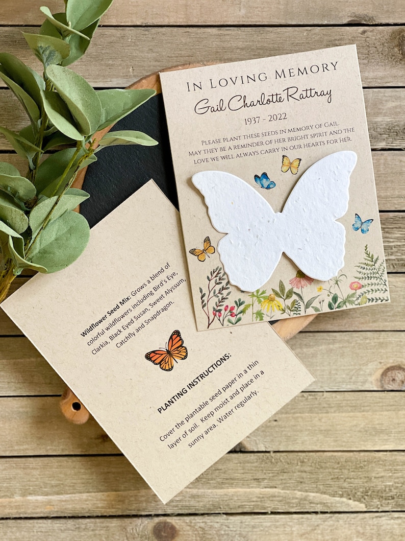 Peut inclure: Une carte brune avec un papier de graines en forme de papillon blanc. La carte indique "En souvenir affectueux Gail Charlotte Rattray 1937-2022 Veuillez planter ces graines en m&eacute;moire de Gail Qu'elles soient un rappel de son esprit lumineux et de l'amour que nous porterons toujours dans nos c&oelig;urs pour elle." Le dos de la carte indique "M&eacute;lange de graines de fleurs sauvages : Fait pousser un m&eacute;lange de fleurs sauvages color&eacute;es, notamment l'&OElig;il d'oiseau, la Clarkia, la Suzanne aux yeux noirs, l'Alysson doux, la Catchfly et le Muflier. Instructions de plantation : Recouvrir le papier de graines plantable d'une fine couche de terre. Garder humide et placer dans un endroit ensoleill&eacute;. Arroser r&eacute;guli&egrave;rement."
