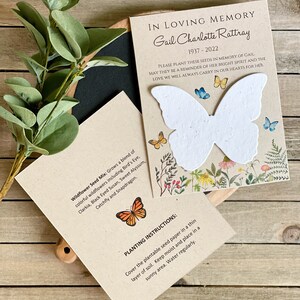 Peut inclure: Une carte brune avec un papier de graines en forme de papillon blanc, entour&eacute; de fleurs et de verdure. La carte indique "En souvenir affectueux Gail Charlotte Rattray 1937-2022" et "Veuillez planter ces graines en m&eacute;moire de Gail. Qu'elles soient un rappel de son esprit lumineux et de l'amour que nous porterons toujours dans nos c&oelig;urs pour elle."