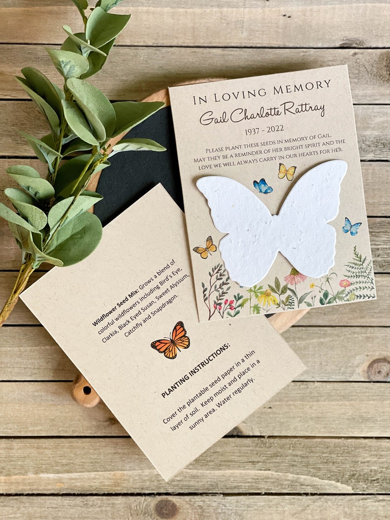 Peut inclure: Une carte brune avec un papier de graines en forme de papillon blanc, entour&eacute; de fleurs et de verdure. La carte indique "En souvenir affectueux Gail Charlotte Rattray 1937-2022" et "Veuillez planter ces graines en m&eacute;moire de Gail. Qu'elles soient un rappel de son esprit lumineux et de l'amour que nous porterons toujours dans nos c&oelig;urs pour elle."