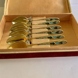 Op de afbeelding: Set van zes gouden theelepels met blauwe en groene emaille-ontwerpen, in een fluwelen doos.