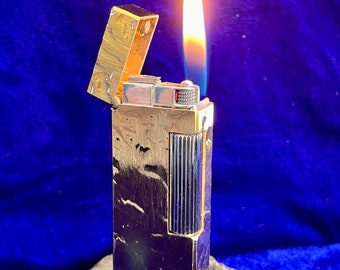 May include: A gold-toned lighter with a textured finish and a silver-toned trim. The lighter is lit and has a flame coming out of the top.