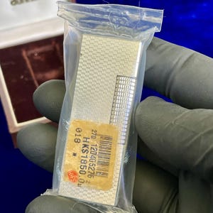 May include: A silver-colored Dunhill lighter in a clear plastic bag. The lighter has a textured pattern and a rectangular shape. A price tag is visible on the lighter. The Dunhill logo is visible on the box.