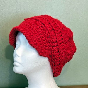 May include: A red crocheted beanie with a wide brim. The beanie is made with a textured stitch and has a slouchy fit.