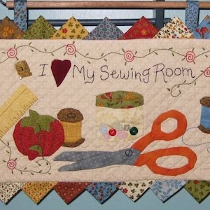 May include: A beige quilted wall hanging with a scalloped border. The centre features the text "I love my Sewing Room" with a red heart and various sewing supplies including scissors, spools of thread, a ruler, and a tomato.