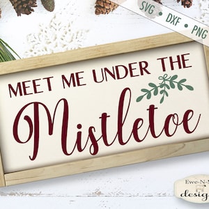 K&ouml;nnte beinhalten: Ein rechteckiges Holzschild mit dem Text "MEET ME UNDER THE Mistletoe" in burgunderfarbener Schrift. Das Schild hat einen cremefarbenen Hintergrund und einen hellbraunen Holzrahmen. Gr&uuml;ne Mistelzweige befinden sich &uuml;ber dem Wort "Mistletoe".