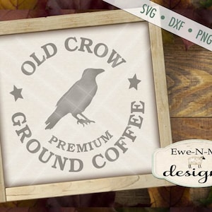 Puede incluir: Un letrero de madera con fondo blanco y el texto "OLD CROW GROUND COFFEE" en un círculo con una silueta de cuervo en su interior. El texto "PREMIUM" está debajo del cuervo. El letrero está sobre una superficie de madera con hojas de otoño.