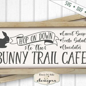 Puede incluir: Un letrero de madera con el texto "Hop on down to the Bunny Trail Cafe" y un conejo de dibujos animados. El letrero tambi&eacute;n enumera los art&iacute;culos del men&uacute;: Sopa de zanahoria, ensaladas frescas y chocolates.