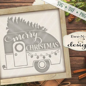 May include: A gray camper with a Christmas tree on top and the words "merry christmas" on the side. The camper has a wreath on the door and lights around the windows.