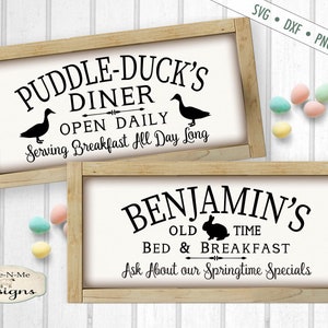 May include: Two wooden signs with black text and graphics. The top sign says "Puddle-Duck's Diner Open Daily Serving Breakfast All Day Long" with a duck illustration. The bottom sign says "Benjamin's Old Time Bed & Breakfast Ask About Our Springtime Specials" with a rabbit illustration.