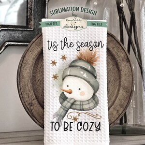 Pode incluir: Toalha de cozinha branca com um desenho de boneco de neve em aquarela. O boneco de neve est&aacute; usando um chap&eacute;u e uma echarpe cinzas. O texto "tis the season to be cozy" est&aacute; impresso na toalha.