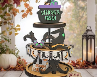 May include: A laser-ready witchy tiered tray set with a cauldron that reads "Witches Brew". The set includes witch hats, boots, and a banner with moons and stars. The tray is made of wood and is perfect for Halloween.