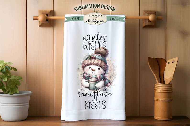 May include: A white kitchen towel with a winter-themed design featuring a snowman holding a cup of hot chocolate. The text on the towel reads "winter wishes snowflake kisses".