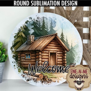 May include: A round sublimation design featuring a watercolor illustration of a log cabin in the woods. The cabin has a wooden door and windows, and there is smoke coming from the chimney. The text "Welcome" is written in black below the cabin. The design is surrounded by a white background with a blue watercolor wash.