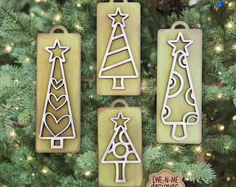 Peut inclure: Ensemble de quatre décorations de sapin de Noël prêtes pour le laser. Chaque ornement en bois présente un motif de sapin découpé et une étoile. Le texte "LASER-READY TREE ORNAMENT SET" est visible en haut.