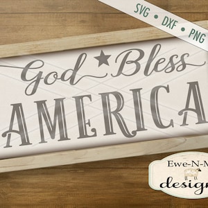 K&ouml;nnte beinhalten: Ein gerahmtes Schild mit wei&szlig;em Hintergrund und Holzrahmen. Das Schild sagt "God Bless America" in einer dekorativen Schriftart mit einem Stern &uuml;ber dem Wort "Bless".