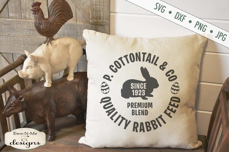 Puede incluir: Una almohada blanca con un dise&ntilde;o circular negro que dice "P. Cottontail & Co. Quality Rabbit Feed Since 1923 Premium Blend". El dise&ntilde;o tambi&eacute;n incluye una silueta de un conejo y dos huevos de Pascua.