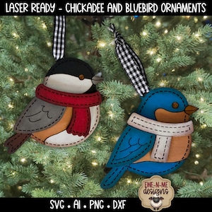 May include: Two laser-ready bird ornaments: a chickadee and a bluebird. The chickadee has a black head, grey wings, and a red scarf. The bluebird is blue with a white scarf. Both have black and white checkered ribbons for hanging.