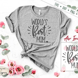 May include: A grey t-shirt with the text "WORLD'S Best MOM" in black lettering. The shirt is displayed on a white surface with pink flowers and green leaves.