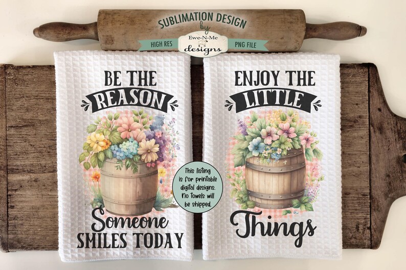 May include: Two white kitchen towels with floral designs and text. The first towel says "Be the reason someone smiles today" and features a floral arrangement in a wooden bucket. The second towel says "Enjoy the little things" and features a similar floral arrangement in a wooden bucket.